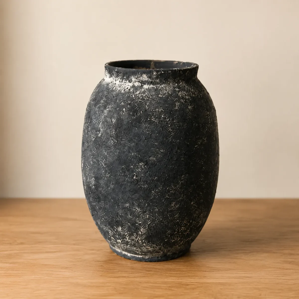 کوزه سفالی پتینه مشکی کهنه کاری شده روی میز چوبی ضخیم با پسزمینه دکوراسیون گرم و نورپردازی ملایم.